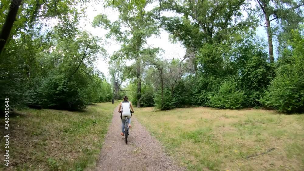 Cycling in the park. Girl riding a bike on a forest trail very quickly. Time lapse. Back view Cycling in the park. Girl riding a bike on a forest trail very quickly. Time lapse. Back view