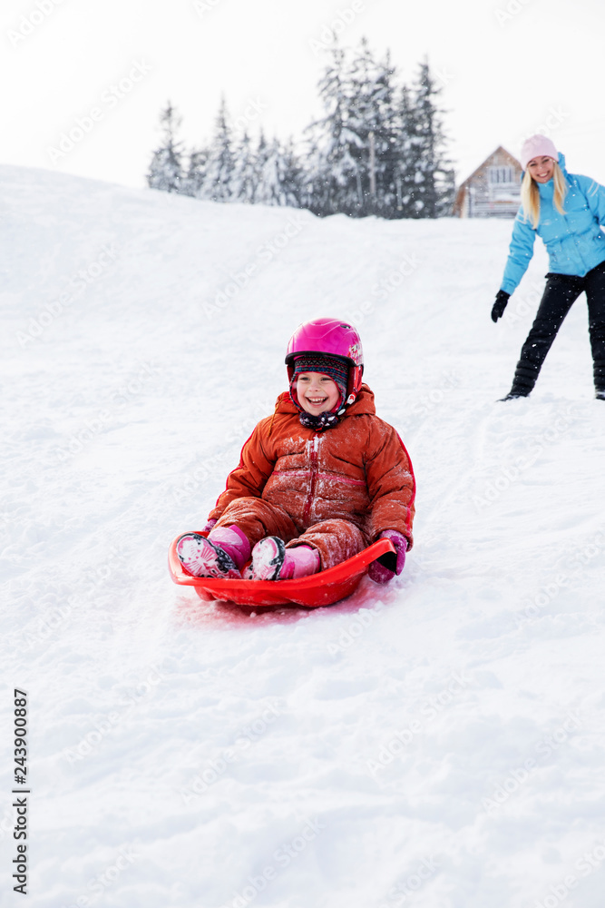 Mom and daughter ride on a sled from a snow slide. Ride from a snow hill on a sled. Sleigh rides, winter fun, snow, family sleigh rides.