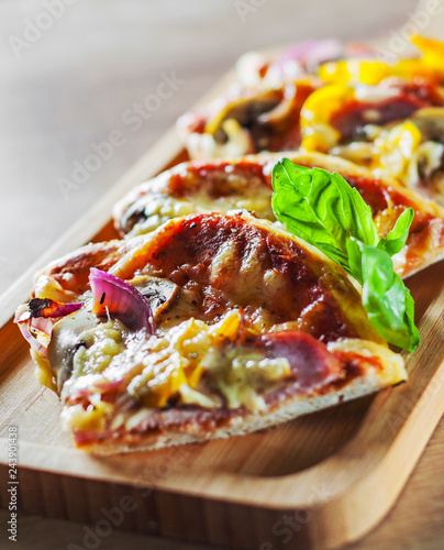 sliced Greek pizza with mushrooms, ham, cheese, onions, pepper on wooden board
