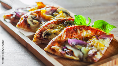 sliced Greek pizza with mushrooms, ham, cheese, onions, pepper on wooden board