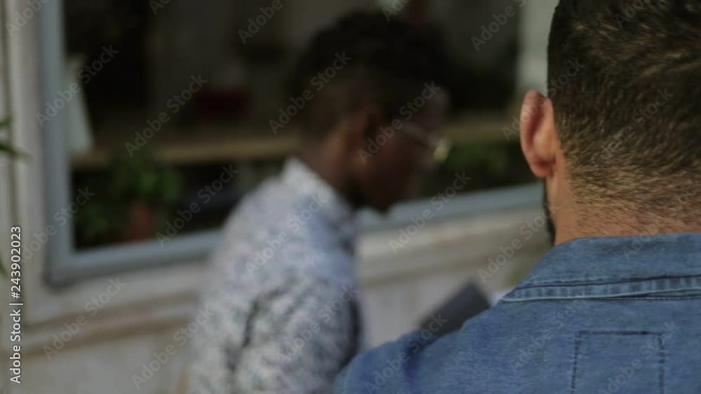 Multiethnic men using laptop and smartphone in outdoor cafe. Young freelancers sitting at table with digital devices and working together in cafe. Remote work concept Multiethnic men using laptop and smartphone in outdoor cafe. Young freelancers sitting at table with digital devices and working together in cafe. Remote work concept