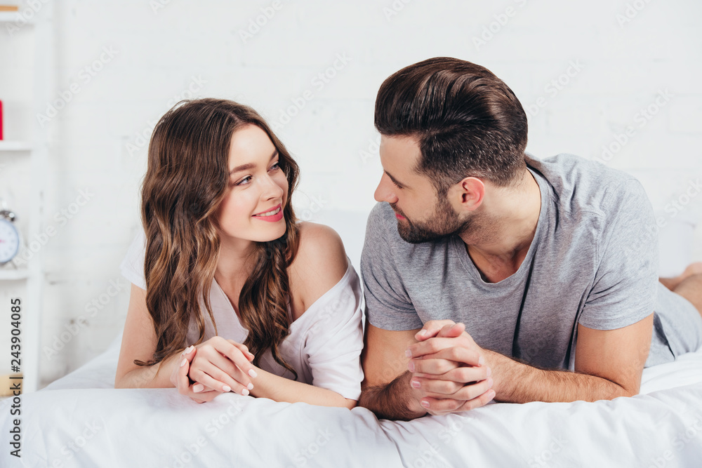 young loving couple lying on soft white bedding young loving couple lying on soft white bedding