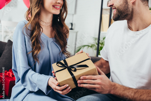 cropped view of young happy couple holding gift box with ribbon
