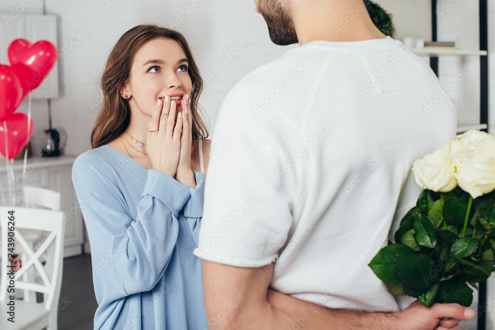 cropped view of a young man holding bouquet of roses behind back while smiling girlfriend waiting for surprise cropped view of a young man holding bouquet of roses behind back while smiling girlfriend waiting for surprise