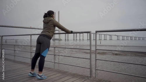 Sporty young woman wuth headphones doing push ups from metal railings. Back view of brunette trainign outdoor. Workout concept photo