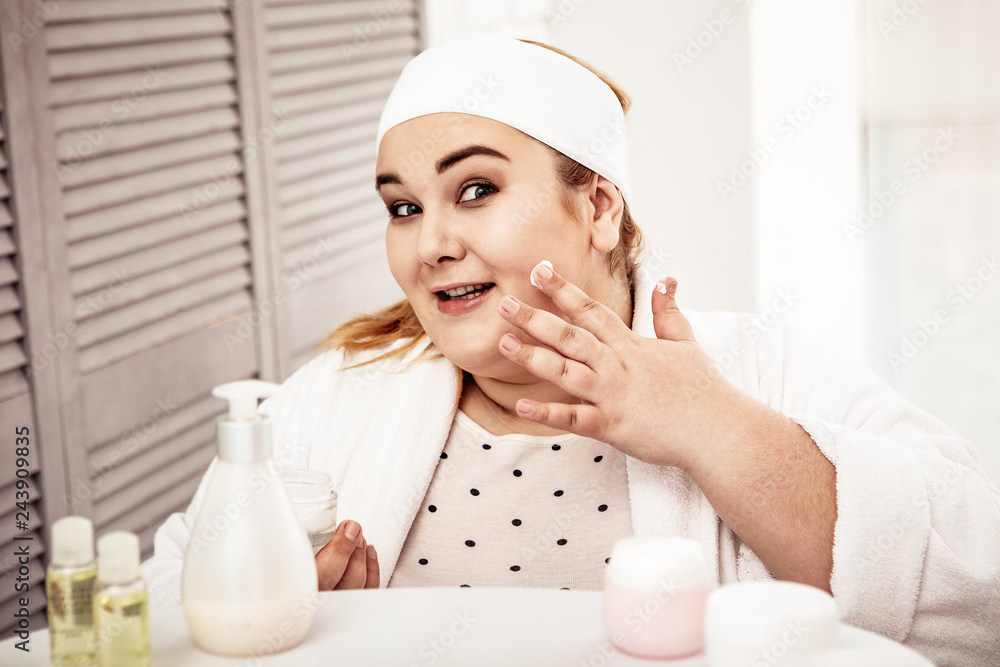 Smiling young overweight woman carrying container with face cream