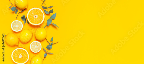 Ripe juicy lemons, orange and green eucalyptus twigs on bright yellow background. Lemon fruit, citrus minimal concept, vitamin C. Creative summer minimalistic background. Flat lay, top view copy space