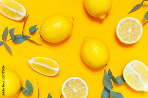 Ripe juicy lemons and green eucalyptus twigs on bright yellow background. Lemon fruit, citrus minimal concept. Creative summer food minimalistic background. Flat lay, top view, pattern photo