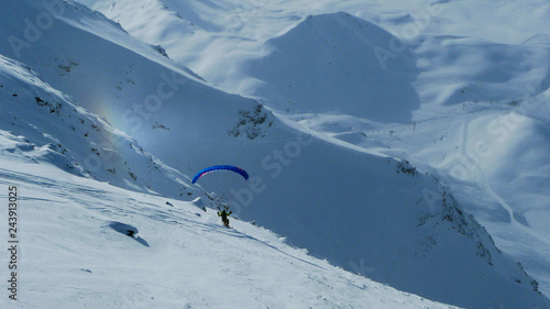 Paraglider starts flying in the mountains, skiing on a slope against the background of a small rainbow effect, Les Arcs
