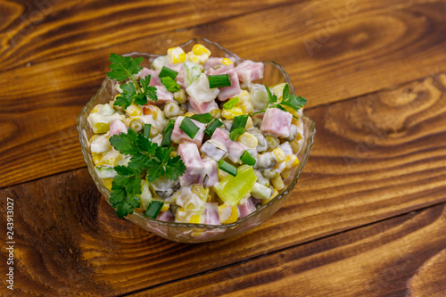 Tasty salad with sausage, green pea, canned corn, bell pepper, cucumber and mayonnaise on wooden table