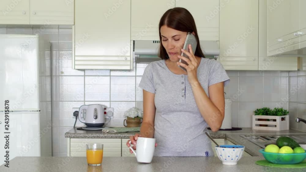 Young woman in pajamas talking on mobile phone. Professional female freelancer receiving good news excited happy cheerful. Female enjoying morning standing on kitchen. Success and achievement concept Young woman in pajamas talking on mobile phone. Professional female freelancer receiving good news excited happy cheerful. Female enjoying morning standing on kitchen. Success and achievement concept