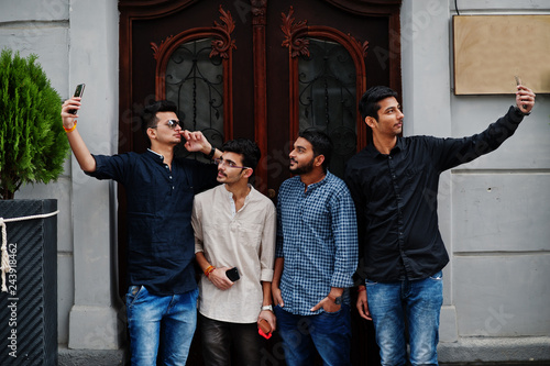 Group of four indian ethnicity friendship togetherness mans. Technology and leisure, guys with phones. Making selfie. photo