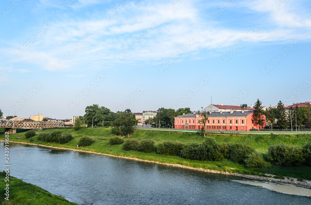 Obraz premium View of the San River. Przemysl - Polish city on the border with Ukraine. Peyziz. A traveler will fall in love with this river, greenery along the banks, a beautiful building on the right. Blue sky wi