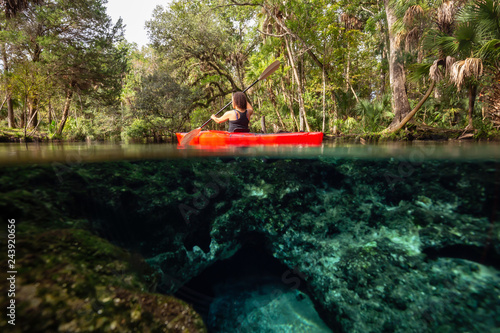 Over and Under picture of a girl kayaking in a lake near an underwater cave formation. Taken in 7 Sisters Springs, Chassahowitzka River, Florida, United States of America.