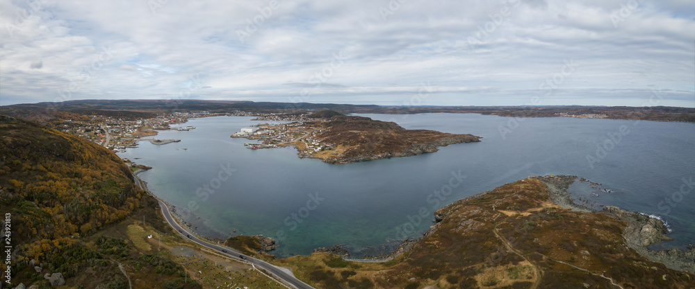 Aerial panoramic view of a small town on a rocky Atlantic Ocean Coast during a cloudy day. Taken in St. Anthony, Newfoundland, Canada.