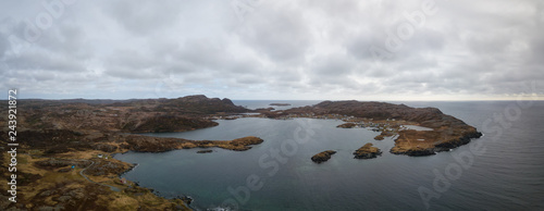 Aerial panoramic view of a small town on a rocky Atlantic Ocean Coast during a cloudy day. Taken in Goose Cove East, near St. Anthony, Newfoundland, Canada.