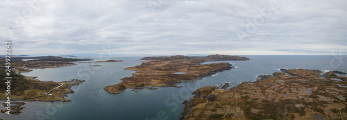 Aerial panoramic view of a small town on a rocky Atlantic Ocean Coast during a cloudy day. Taken in Quirpon, Newfoundland, Canada.