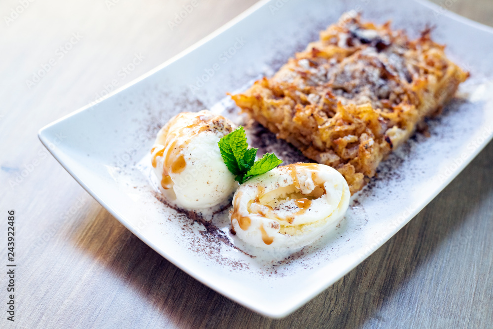 Delicious fresh dessert with green mint leaves, sprinkled with powdered sugar, is on the table in a white rectangular plate.