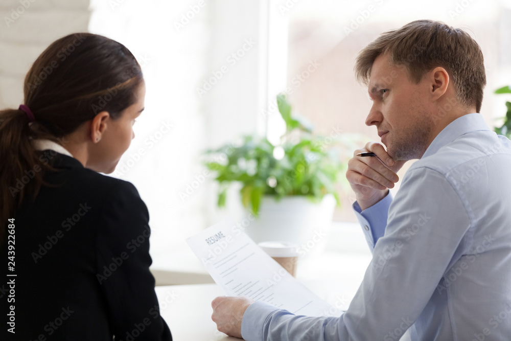 Doubting hr manager looking at applicant at job interview rear view, job seeker answering at employer question, man attentively listen woman, holding resume in hand, thinking about hiring decision Doubting hr manager looking at applicant at job interview rear view, job seeker answering at employer question, man attentively listen woman, holding resume in hand, thinking about hiring decision