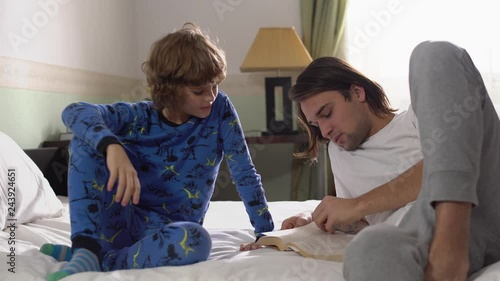 Two brothers lie down in bed, older brother read for small brother a book and high five photo