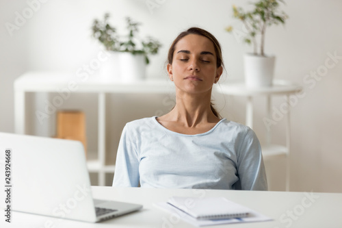 Calm attractive woman relaxing at workplace, sitting with closed eyes, leaning back in chair, meditating at work, deep breath, no stress concept, businesswoman, student resting after finish work