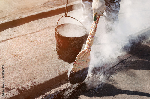 Worker repairs the roof with molten tar from a bucket with a broom.
