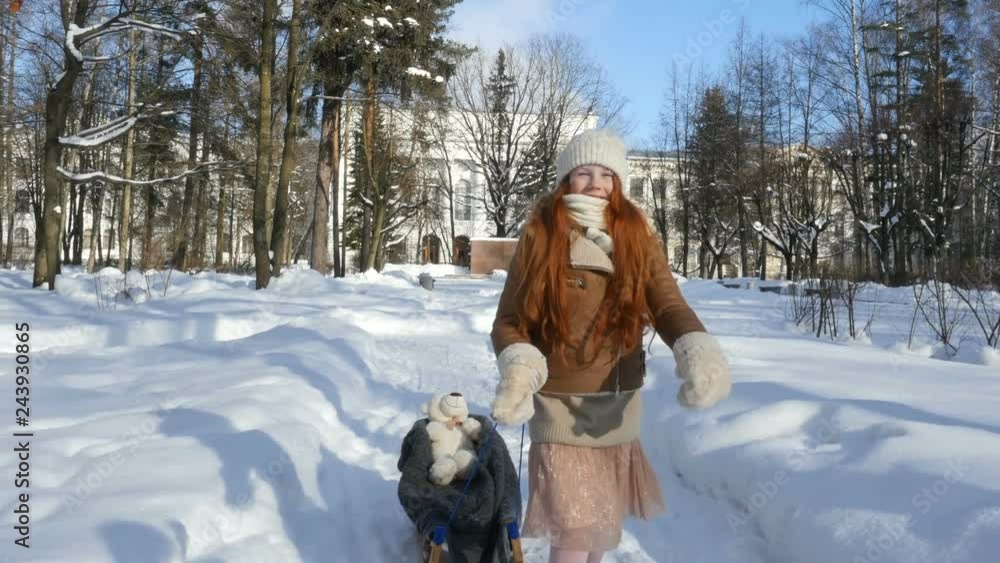 Red-haired child, little girl running with sledge on winter park. Child walking and playing on winter sunny day Red-haired child, little girl running with sledge on winter park. Child walking and playing on winter sunny day