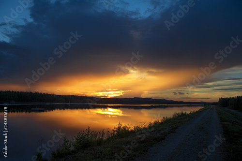 Sunset on the river. Single lane road leading through landscape.