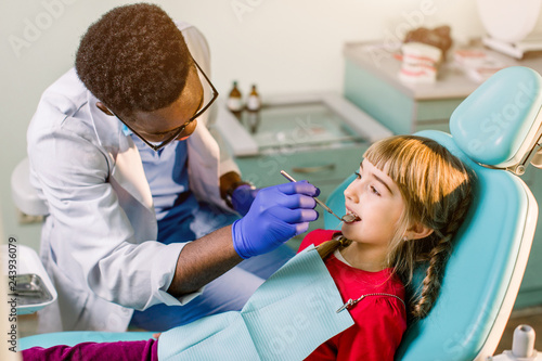 Children s dentistry  Pediatric Dentistry. A male African-American stomatologist is treating teeth of a school-age girl. Oral health and hygiene
