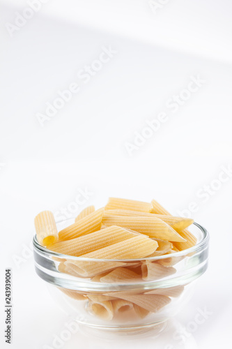 Raw feathers macaroni in bowl. Italian pasta close up on the white background