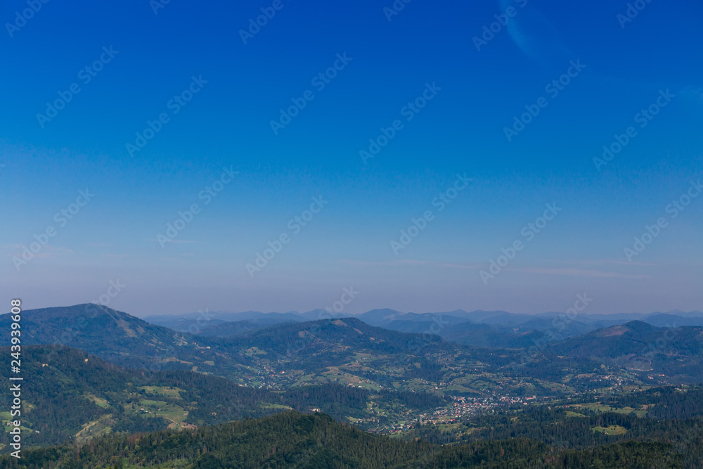 many mountains covered with green forests and a horizon that separates mountains and blue sky. a small village in the valley of the mountains