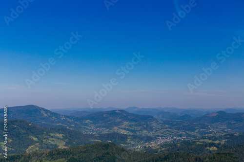 many mountains covered with green forests and a horizon that separates mountains and blue sky. a small village in the valley of the mountains