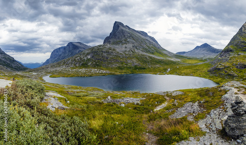 Beautiful mountain scenery with lake near Trollstigen road from Andalsnes to Stranda in Norway, Scandinavia. Panoramic summer landscape with green grass and large picturesque stones in the foreground.