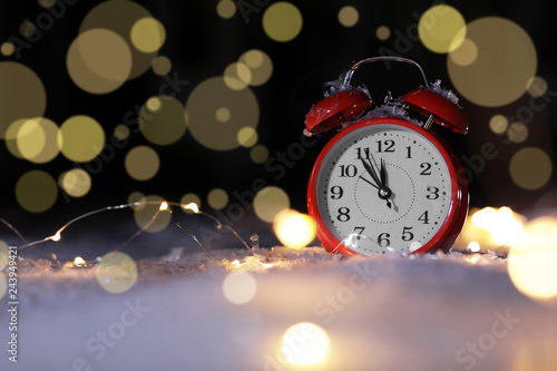 Alarm clock and Christmas lights on snow against blurred background, space for text. Winter night