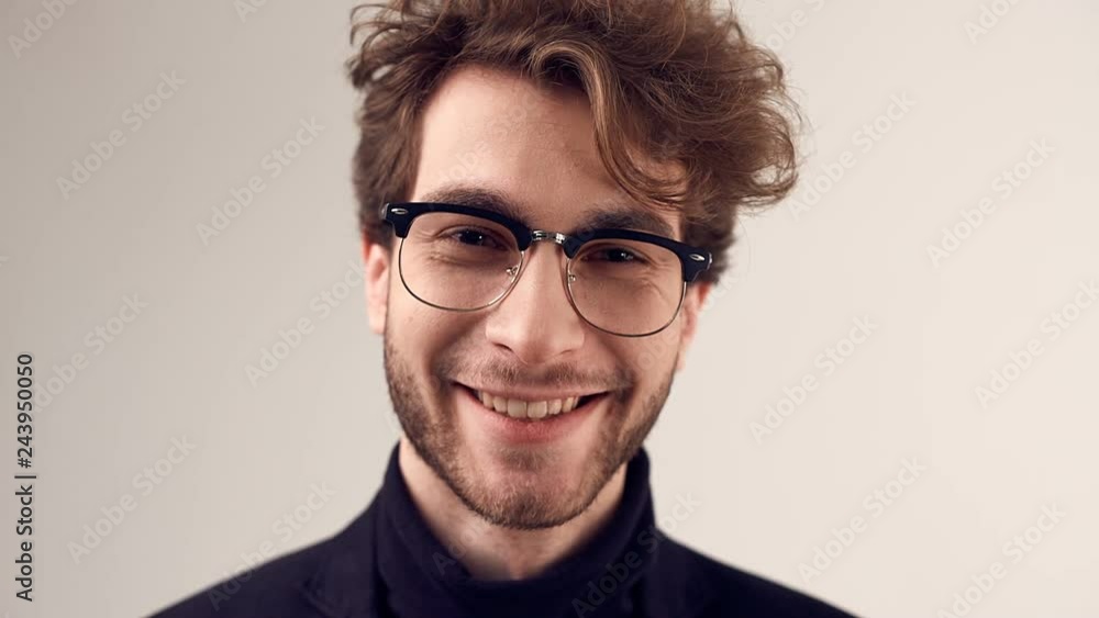 Fashion portrait of handsome elegant man with curly hair wearing suit and glasses on gray background in studio Fashion portrait of handsome elegant man with curly hair wearing suit and glasses on gray background in studio