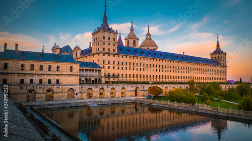 Sunset behind the beautiful El Escorial palace and monastery at the San Lorenzo de El Escorial with the Frailes Garden and reflections in the pond. Famous kings residence near Madrid in Spain