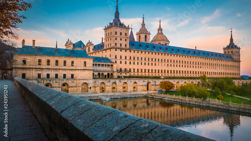 Street with colorful trees in fall, autumn next to the beautiful El Escorial palace and monastery at the San Lorenzo de El Escorial during sunset, dusk. Famous kings residence near Madrid in Spain