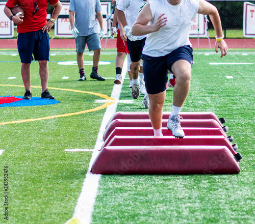 Fotografie Footaball player running over barriers at preseason practice
