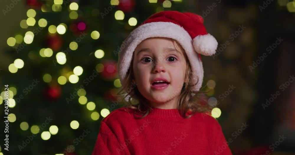 The slow motion of cute cheerful little girl wearing santa hat singing a Christmas Song with sparklers in her hands. Shot with RED camera in 8K. Concept of Christmas time, winter holidays, family fun. The slow motion of cute cheerful little girl wearing santa hat singing a Christmas Song with sparklers in her hands. Shot with RED camera in 8K. Concept of Christmas time, winter holidays, family fun.