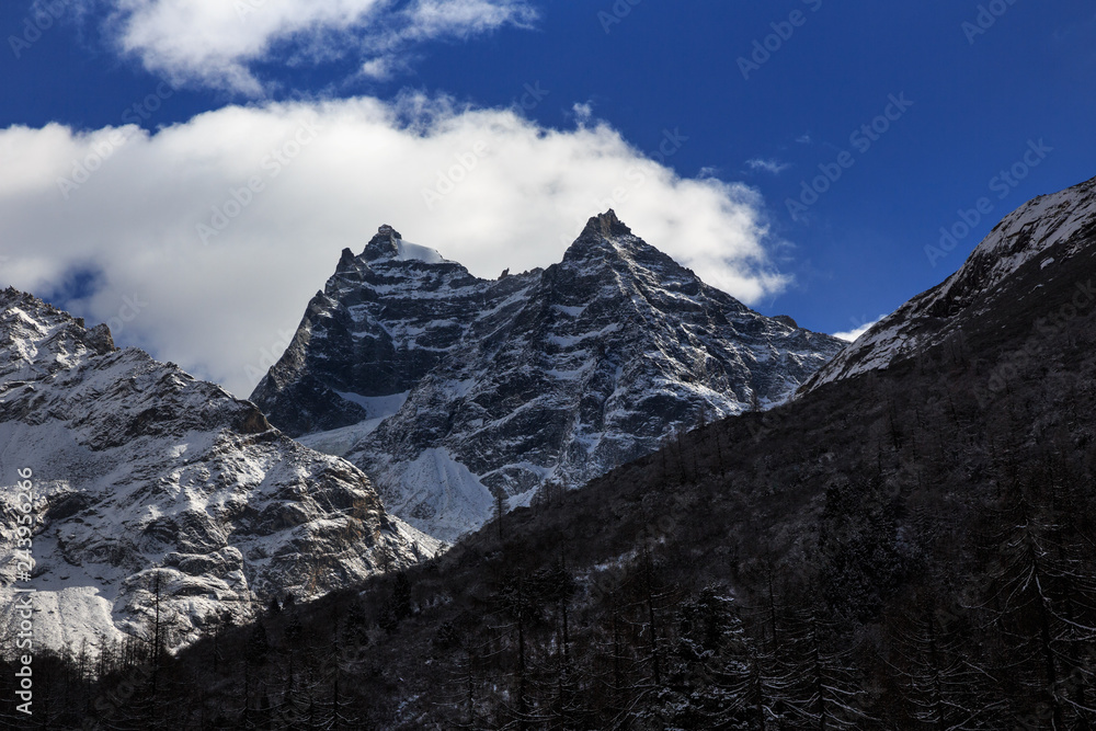 Four Girls Mountain National Park in Sichuan Province, China. ShuangQiao Valley Scenic Area, Snow Capped Mountains with clouds forming at the summit. Blue Sky, Snow Covered Trees, Siguniangshan
