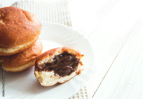 donuts with chocolate filling on white plate, white wooden background copy space