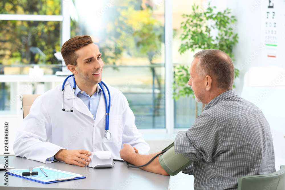Fototapeta premium Doctor measuring blood pressure of mature patient in hospital