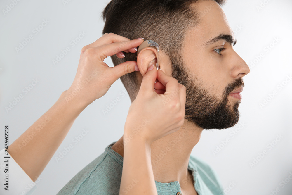 Fototapeta premium Otolaryngologist putting hearing aid in man's ear on white background