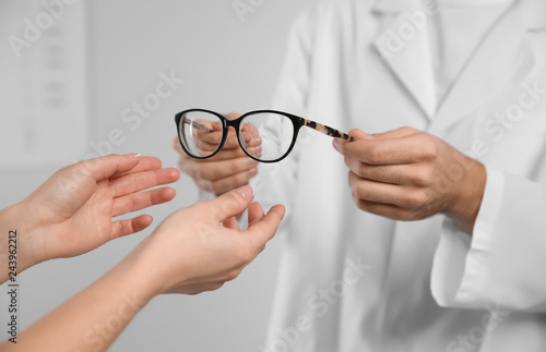 Male ophthalmologist helping woman choose glasses in clinic, closeup