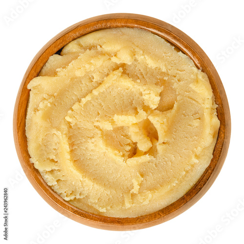 Yellow marzipan paste in wooden bowl. Marzapana or marchpana, made of ground almonds and sugar or honey. Used for sweets and to shape small figures. Food photo closeup from above, on white background. photo