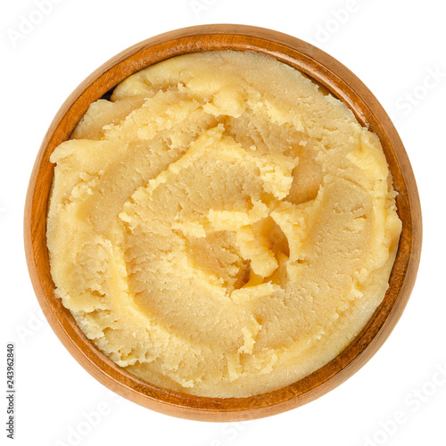 Yellow marzipan paste in wooden bowl. Marzapana or marchpana, made of ground almonds and sugar or honey. Used for sweets and to shape small figures. Food photo closeup from above, on white background.