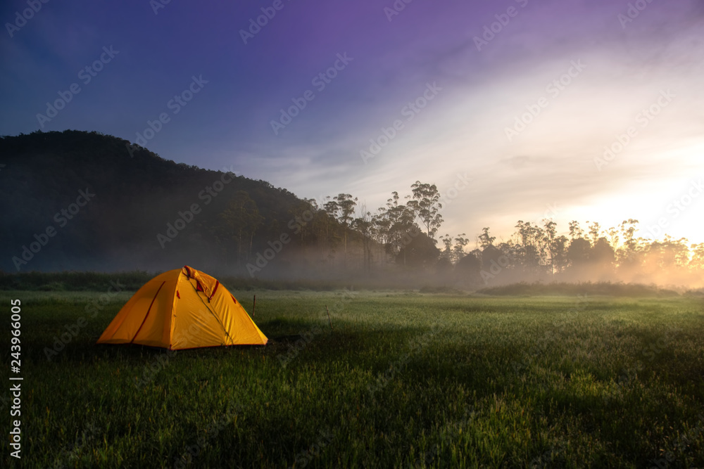 Yellow Camping Tent In The Middle of Open Field Near Forest During Sunrise at Misty Morning. Concept of Outdoor Camping Advanture