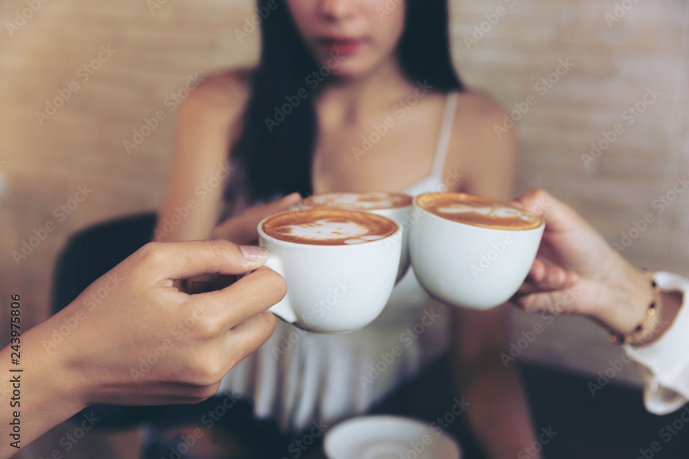 Group of friends cheers with latae cup in cafe bar with phone on table sitting intdoor at cafe - Young girl group having fun drinking together. Group of friends cheers with latae cup in cafe bar with phone on table sitting intdoor at cafe - Young girl group having fun drinking together.