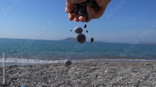 Slow motion Free fall of pebbles from loosen fist, sea view in the background photo