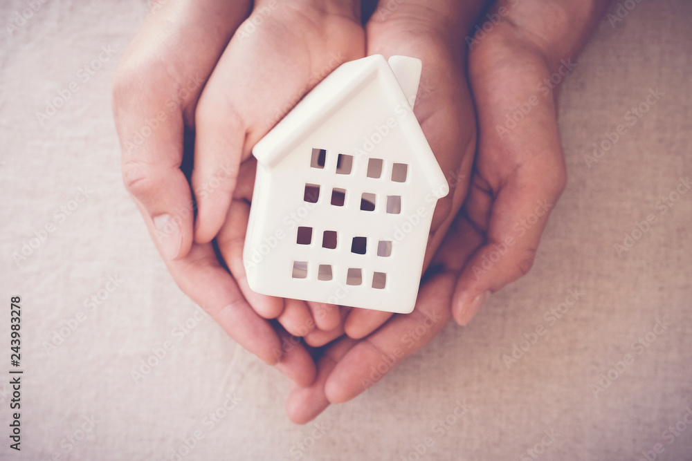 Adult and child hands holding white house, family home and homeless shelter concept Adult and child hands holding white house, family home and homeless shelter concept